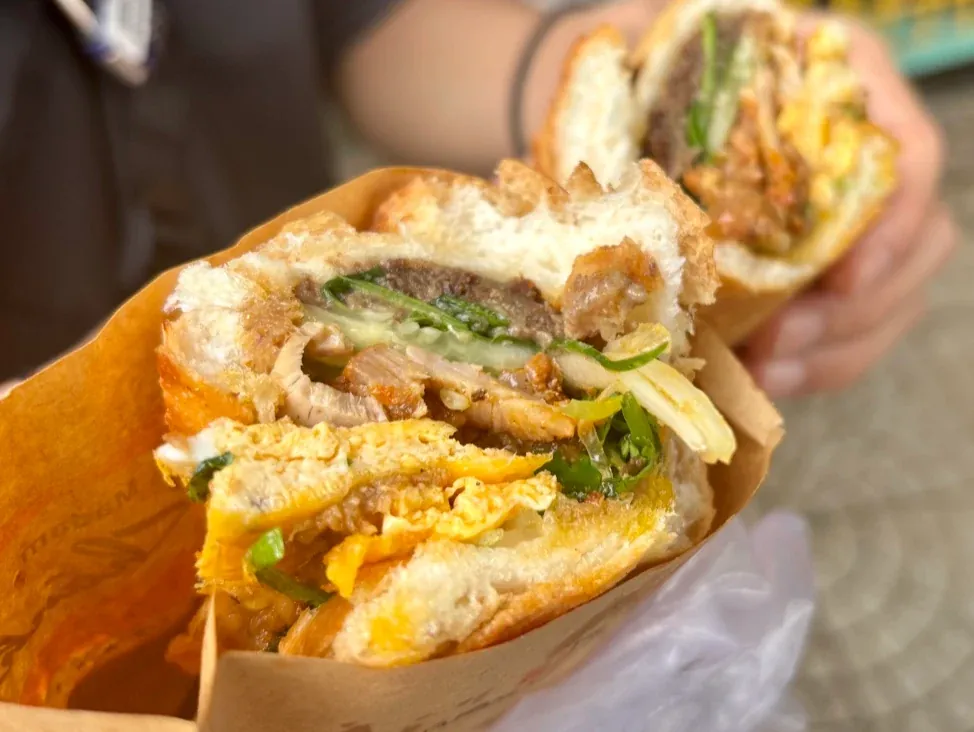 Ổ bánh mì Madam Khánh cắt đôi, lớp trứng chiên, thịt nướng và rau thơm